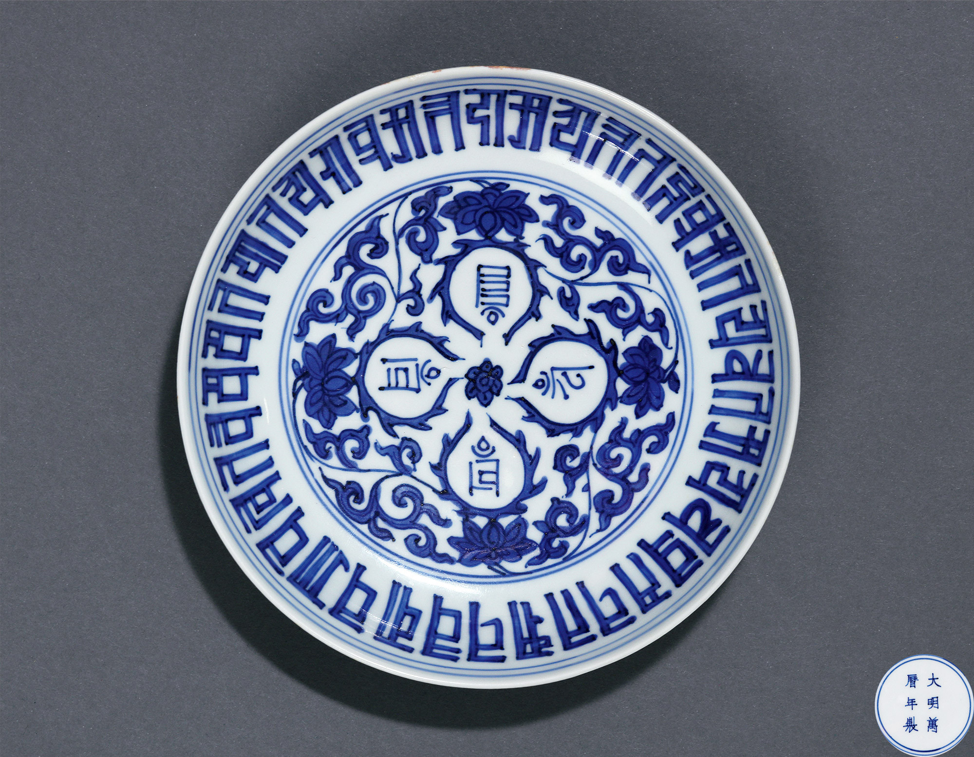 A BLUE AND WHITE PLATE WITH SANSKRIT AND FLOWER DESIGN
